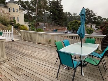 Outdoor patio with glass table, colorful chairs, and closed umbrella on wooden deck.