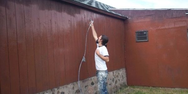 Worker spray painting the outside of barn red