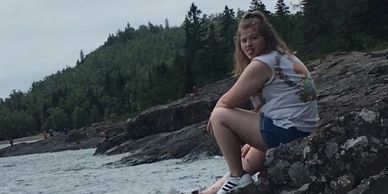 Our current employee, Hannah, sitting on a rock by the water