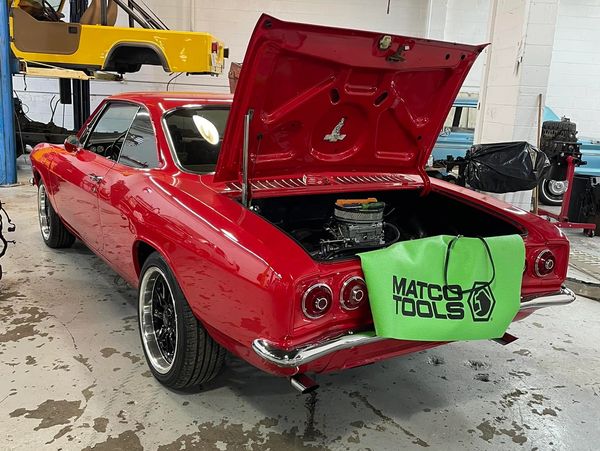 Red classic car with open trunk in a garage, showing engine and tools.