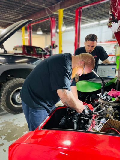 Crew Co mechanics working together on a car engine in a garage.