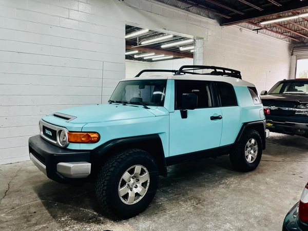 Light blue Toyota FJ Cruiser parked indoors beside a black truck.