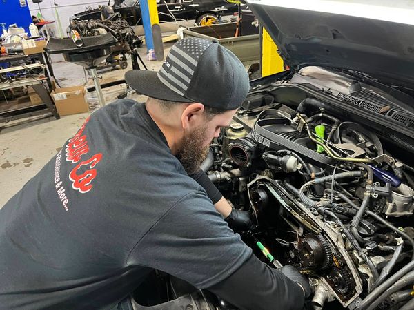 Mechanic working on a car engine in a garage with tools around.