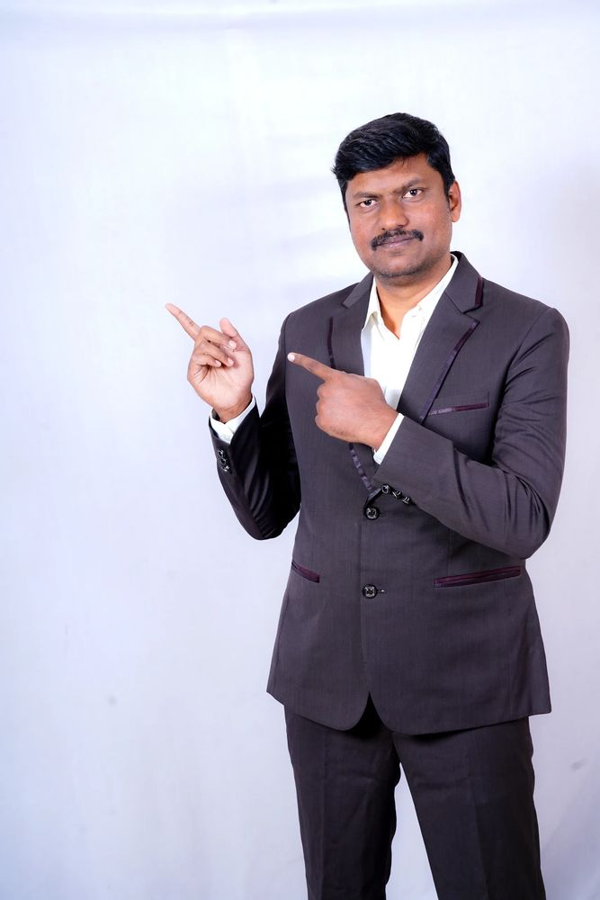Man in a dark suit pointing to the left with both hands.