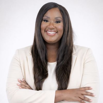 Confident woman smiling with arms crossed in a light blazer.