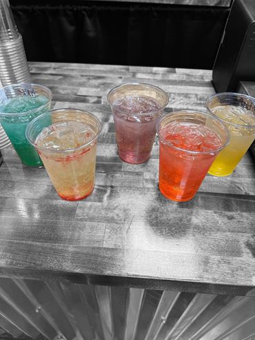 Five colorful iced drinks on a wooden counter with a black and white background.
