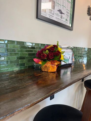 Colorful flower arrangement on a wooden counter with green tile backsplash.