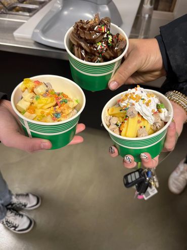 Three hands holding colorful frozen yogurt cups with various toppings.