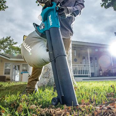 Person using a Makita leaf blower in a yard covered with leaves.