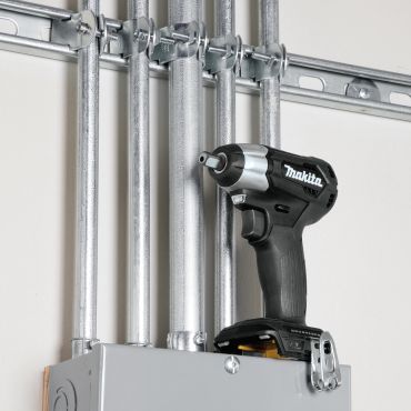 A Makita cordless drill resting on an electrical panel with metal conduit pipes above.