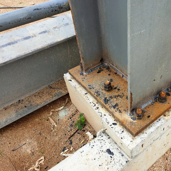 Rusty steel column base with bolts on concrete foundation outdoors.