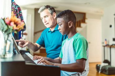 photo of grandparent teaching a boy how to read music at a piano