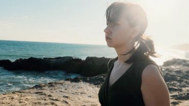 Woman gazing thoughtfully at the ocean on a sunny day.