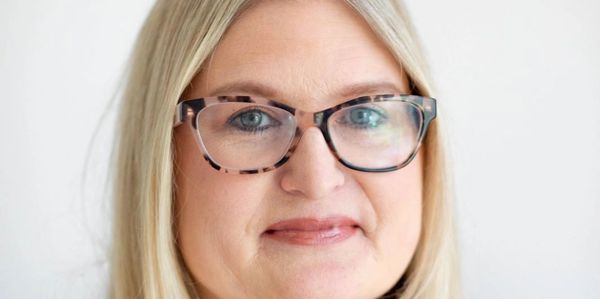 Professional woman with glasses and blonde hair smiling gently.