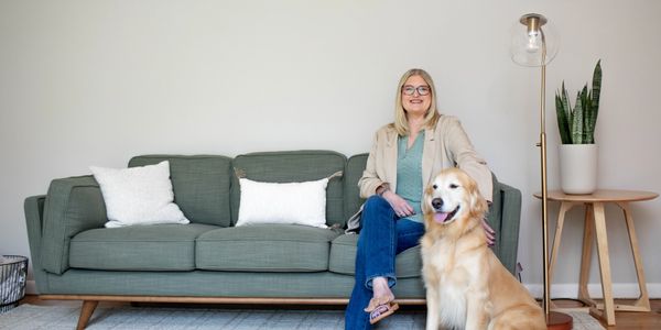 Woman sitting on a green couch with a golden retriever dog beside her.