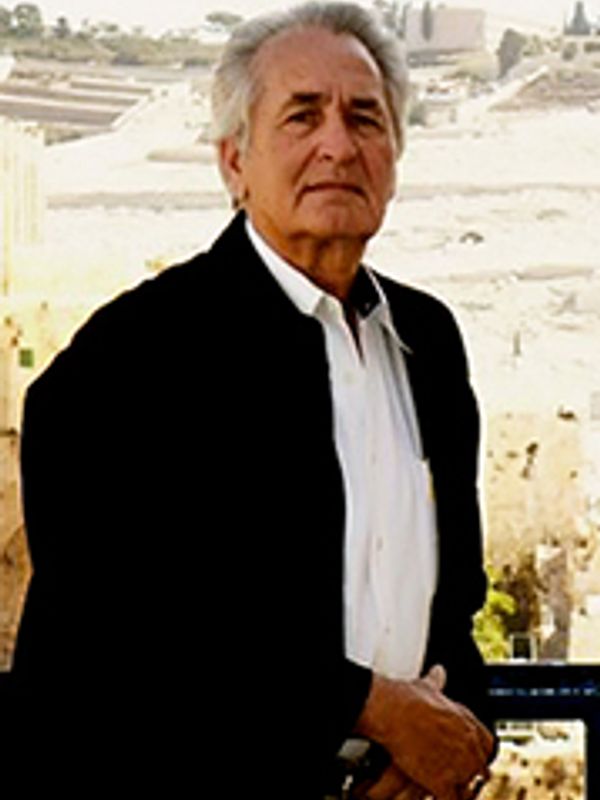 Elderly man standing outdoors with a serious expression.
