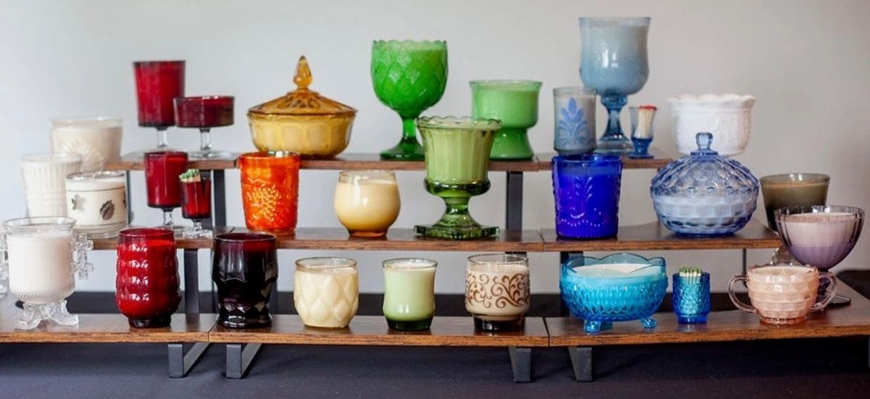 Colorful vintage candle holders arranged on tiered wooden shelves.