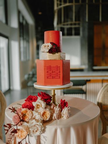 Elegant three-tier red wedding cake with floral decorations on a round table.