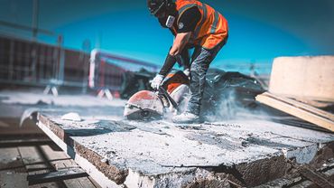 Construction worker cutting concrete with a power saw wearing safety gear.