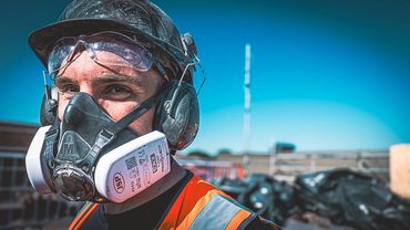 Construction worker wearing safety gear including a mask, helmet, and goggles.