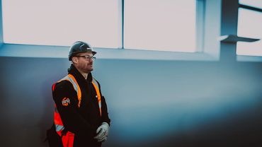 Construction worker in safety gear standing indoors near a large window.