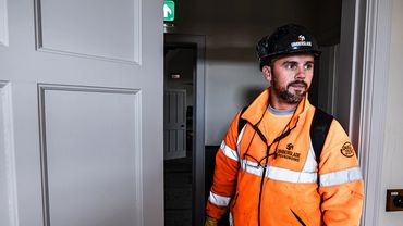 Construction worker in orange safety gear stands inside a building doorway.