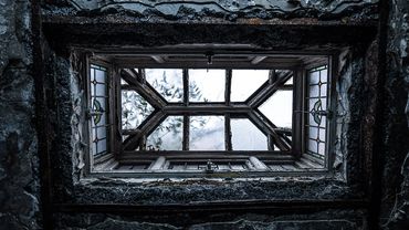 A weathered, stained glass window in an old, decayed building.