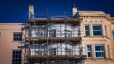 Scaffolding set up on the front of a white building under a clear blue sky.
