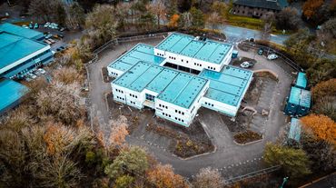 Aerial view of a modern building surrounded by autumn trees and parking areas.