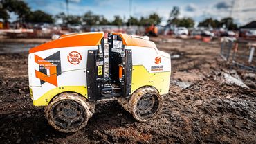 A small, orange and white robotic groundworks vehicle on a muddy construction site.