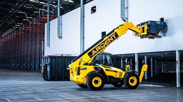 Yellow telehandler lifting a container inside a warehouse.