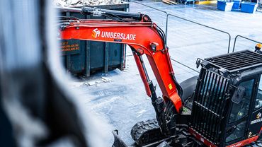 Red and black construction excavator at a worksite with Umberslade branding.