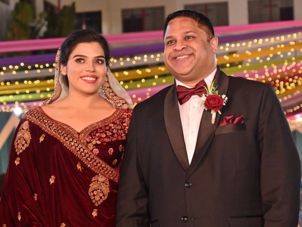 A couple dressed elegantly at a festive event with lights in the background.