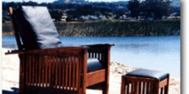 Wooden lounge chair and ottoman by the water on a sandy shore.