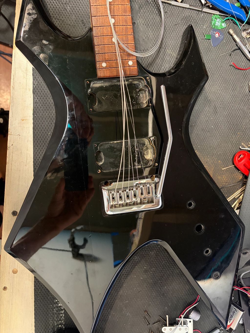Black electric guitar undergoing repair with strings removed.