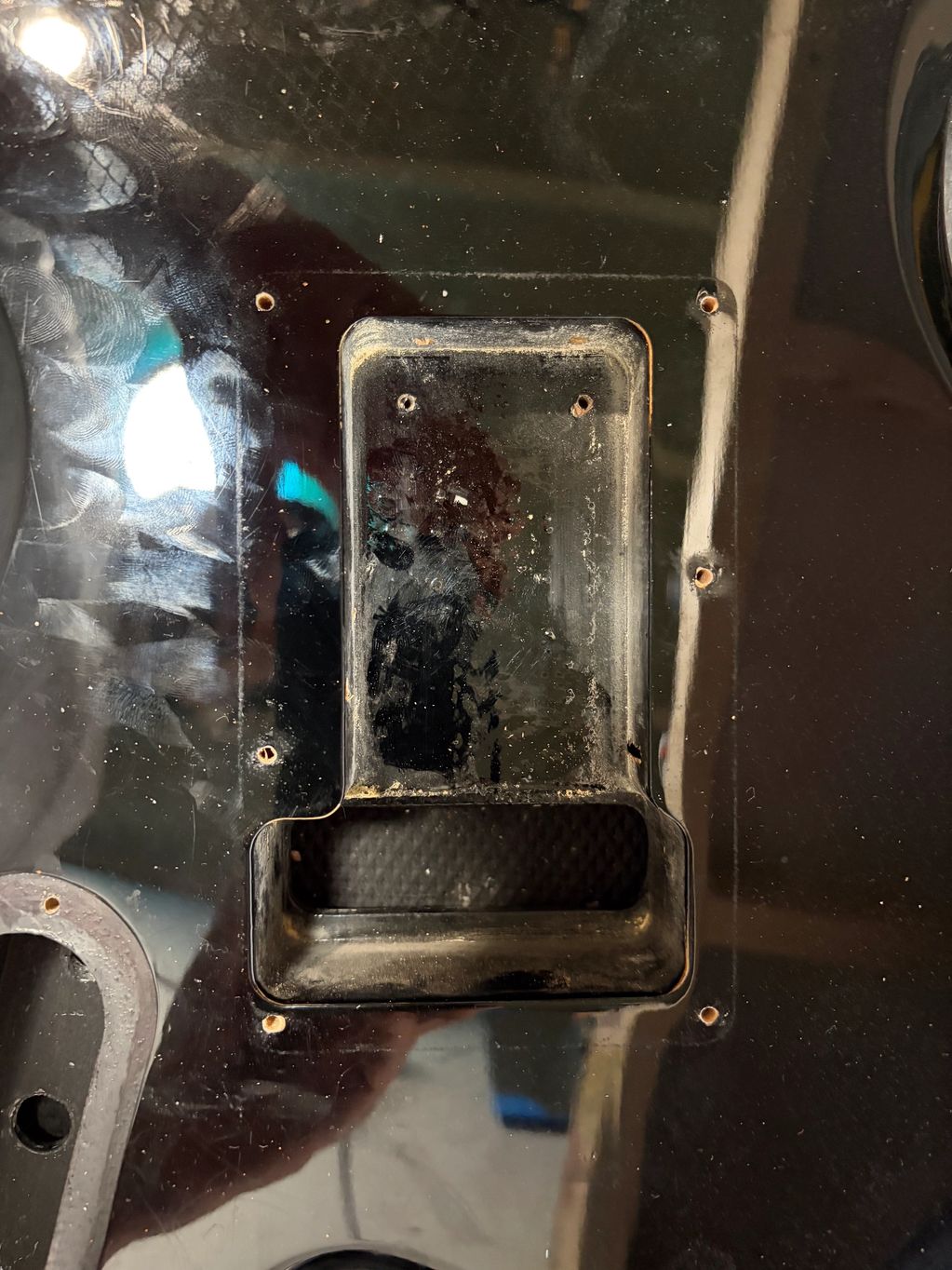 Close-up of a black scratched surface with screw holes and a rectangular cavity.