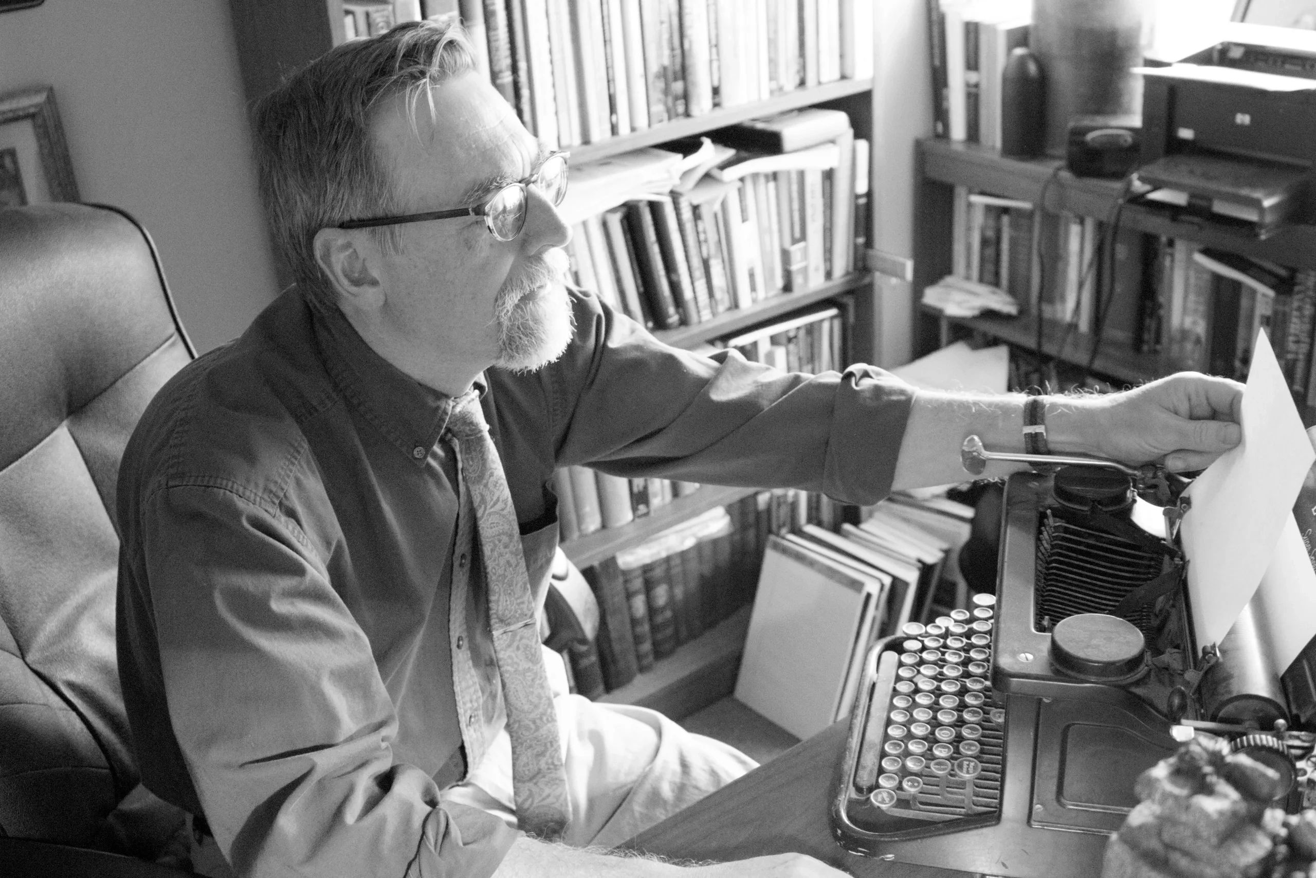 Man using a vintage typewriter in a book-filled office.