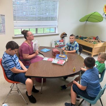 Teacher and children sitting around a table in a classroom.
