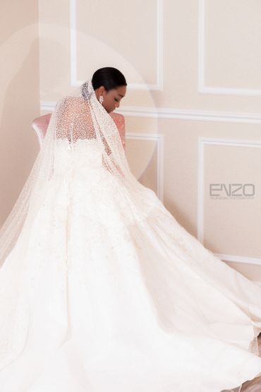 Bride in a stunning white gown and delicate veil sits gracefully on a pink chair.