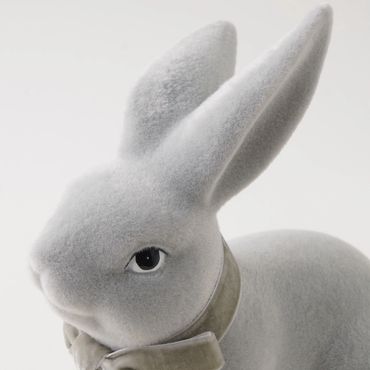 Close-up of a soft, light gray rabbit figurine with a velvet bow around its neck.