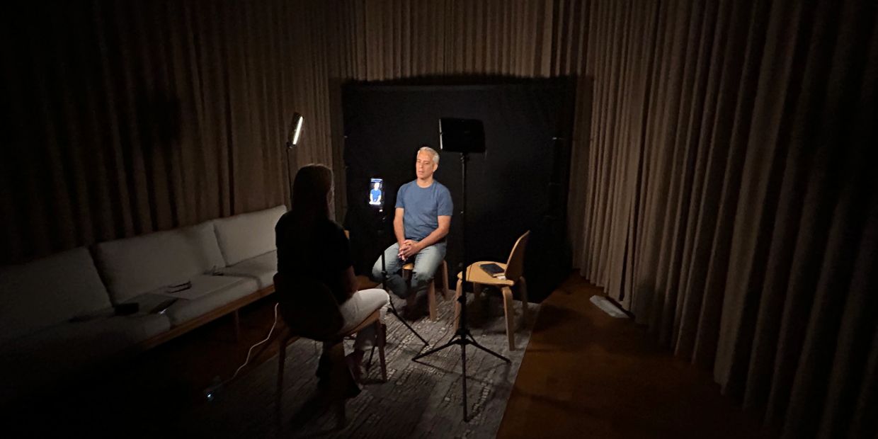 A man is being interviewed in a dimly lit room with professional lighting setup.