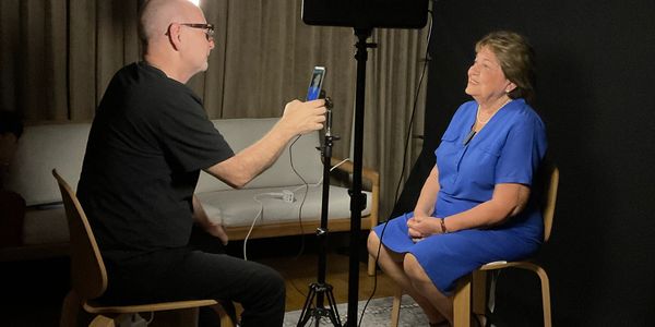 A man films a woman in a blue dress during an interview setup.