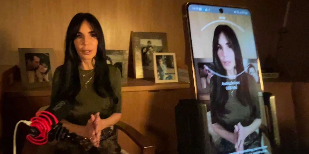 Woman recording a video interview in a dimly lit room with a smartphone.