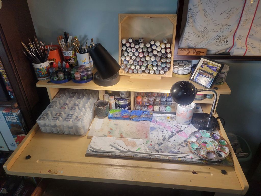 A well-organized artist's workspace with paintbrushes, paints, lamps, and palettes.