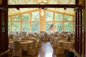 Rustic wooden dining hall with tables set for an event, large windows, and natural light.
