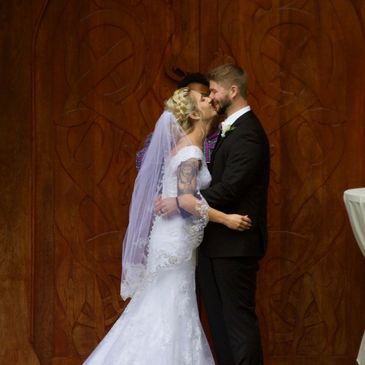 A bride and groom share a kiss in front of a large wooden door during their wedding ceremony.