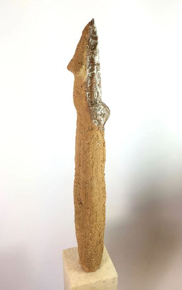 Abstract gold clay figurine on a stand.