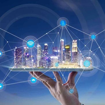 Hand holding a digital tablet projecting a smart city with connected IoT icons.