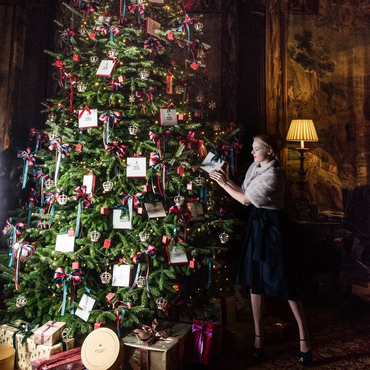 A woman decorating a large Christmas tree with ribbons and gifts.