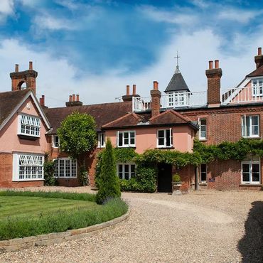 Large traditional brick house with manicured garden and curved driveway under a blue sky.